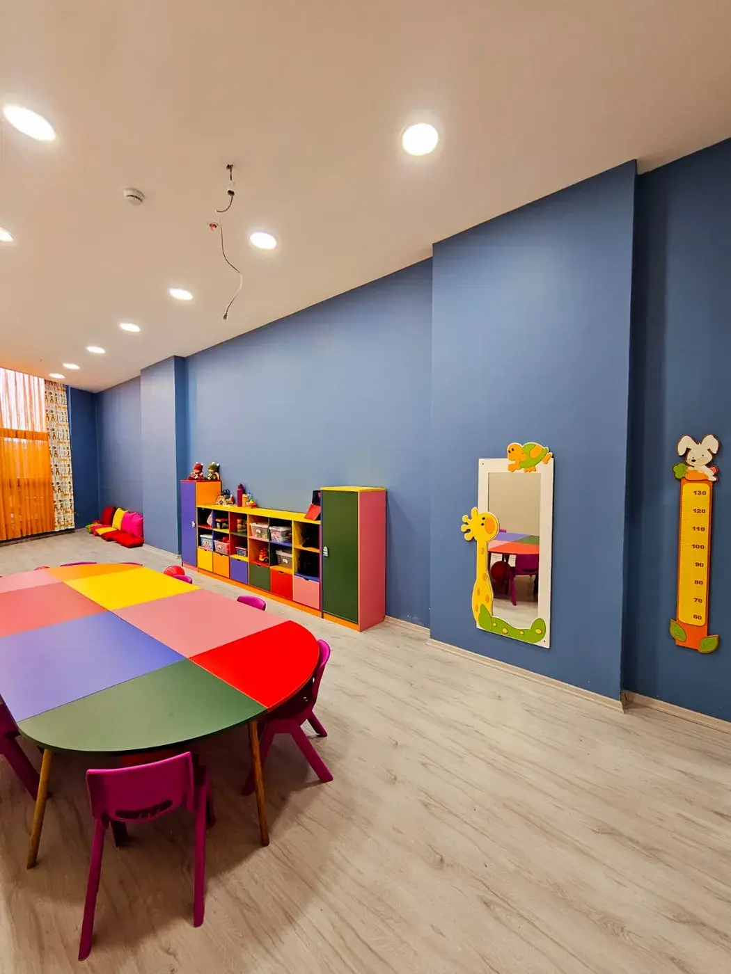 Mavi duvarlı sınıf: renkli masa, aynalı köşe ve boy ölçme cetveli